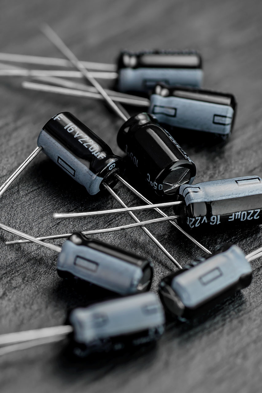 A collection of black and silver electronic capacitors sit scattered on a dark gray surface.